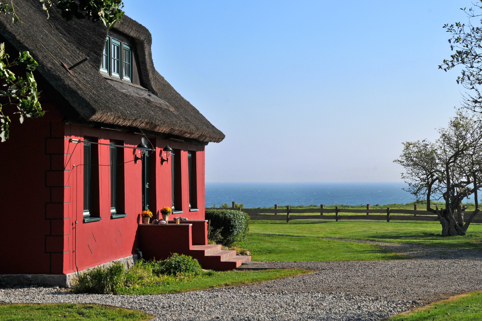 Rotes Ferienhaus mit Reetdach auf Rügen mit Blick auf die Ostsee