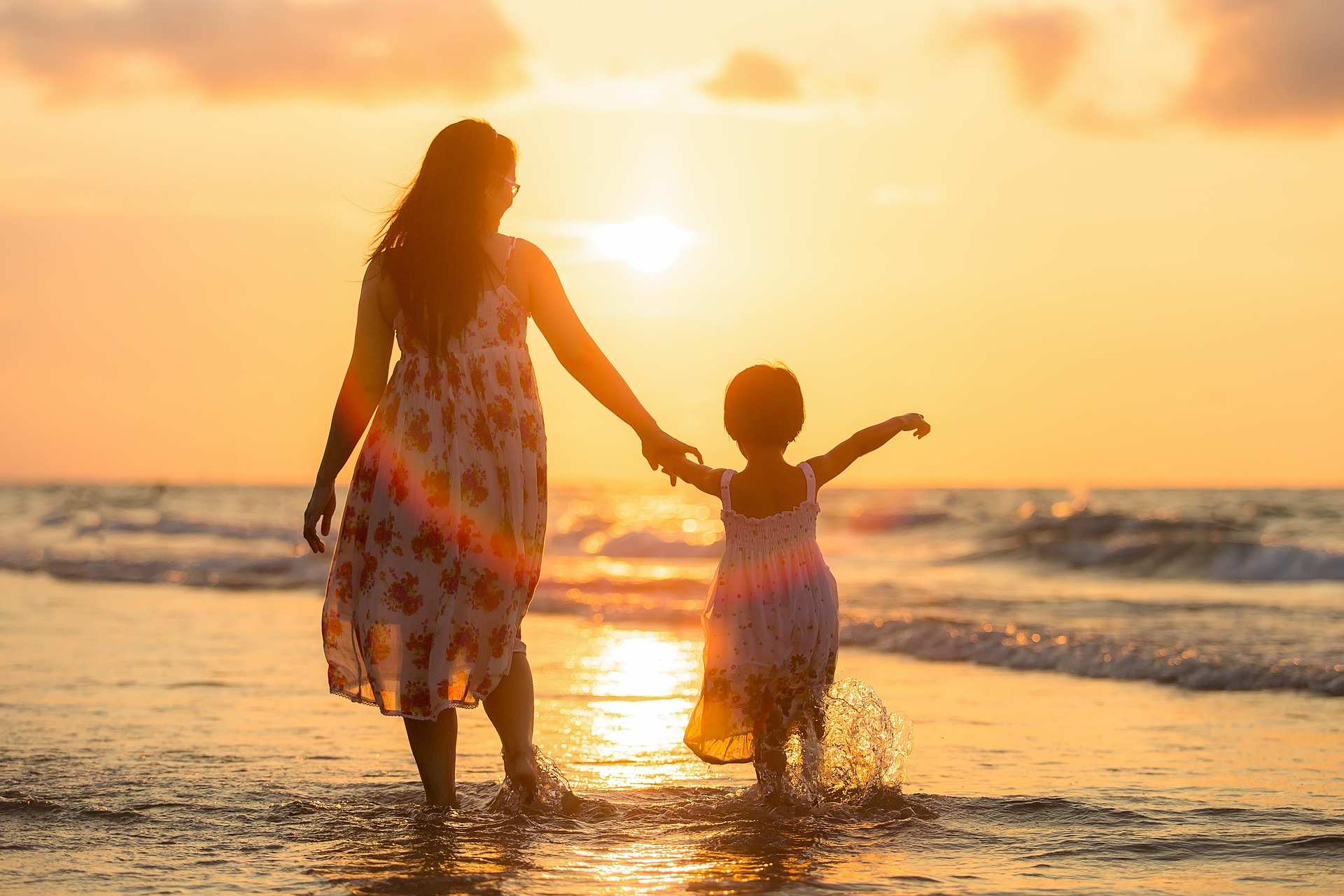 Mutter und Kind an der Hand am Strand bei Sonnenuntergang
